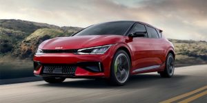 red 2024 Kia EV6 driving on a street with hills in the background