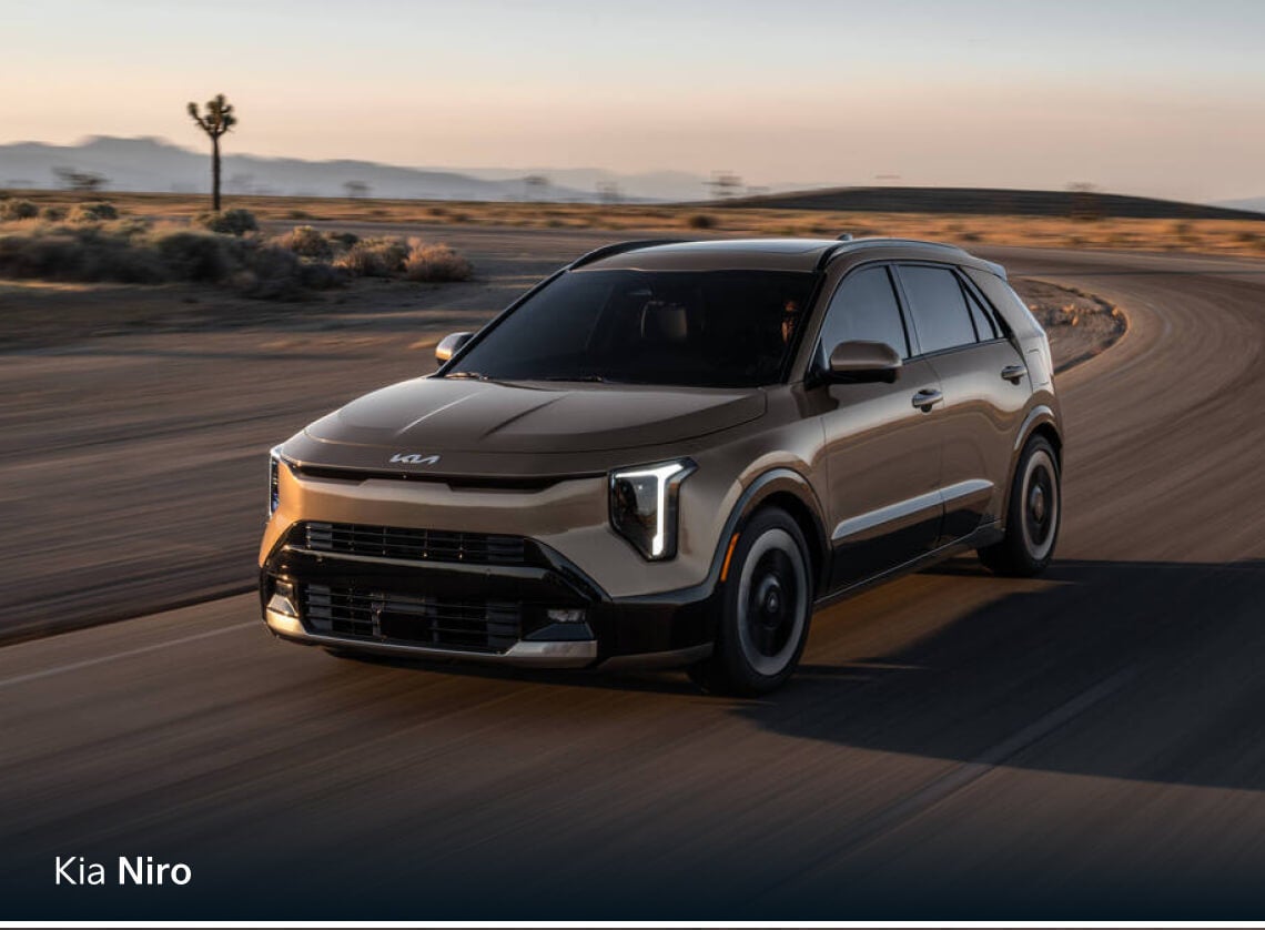 Front three-quarter view of bronze Kia Niro EX driving on a curved desert road.